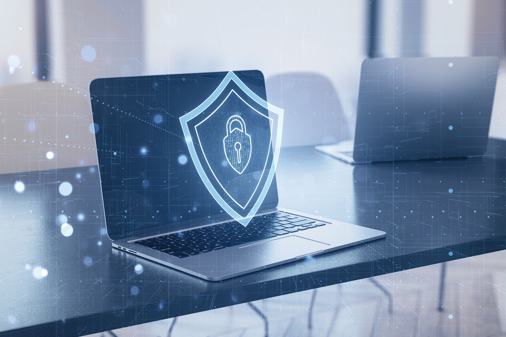 Laptop with a digital shield symbol onscreen signifies cybersecurity concept, blended with an office interior background